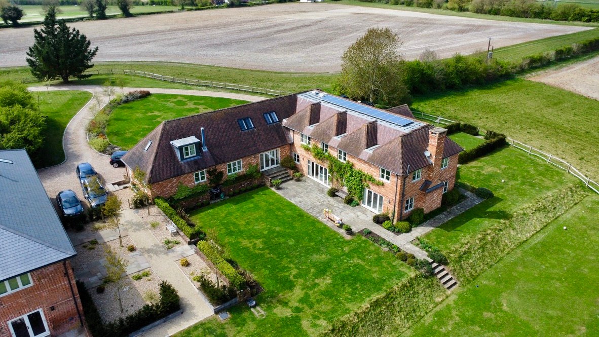 Brick farmhouse with solar panels and surrounding farmland, aerial view